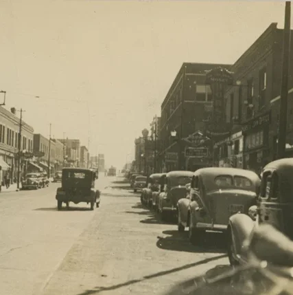 Sepia toned photo of 18th Street at Vine Street. Cars are parked along both sides of the street while a single car drives away from the camera.